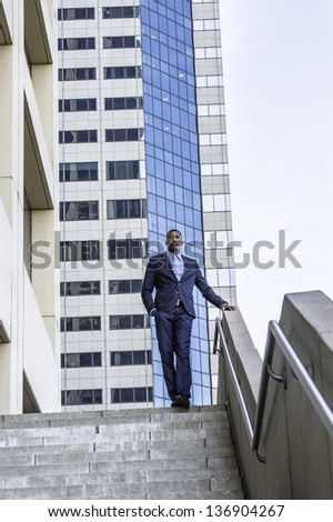 A young handsome black businessman is standing outside of a business building and confidently looking forward./Portrait of Young Black Businessman