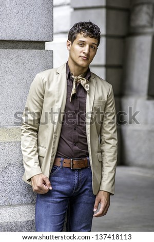 Dressing in a beige color blazer, a coffee color shirt, blue jeans, a scarf tied in the neck, a handsome guy is charmingly looking at you/Portrait of Young Guy