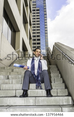 Holding a magazine, a young student is sitting on steps outside a business building and making a phone call./Take  a Break