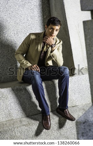 Wearing a watch and touching his chin, a young handsome businessman is sitting outside and thinking./Thinking Outside
