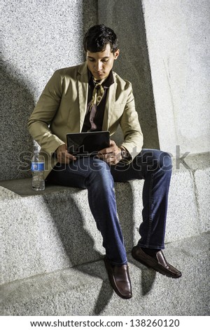 Sitting outside with a bottle of water, a young handsome businessman is  working on a small computer/Working Outside