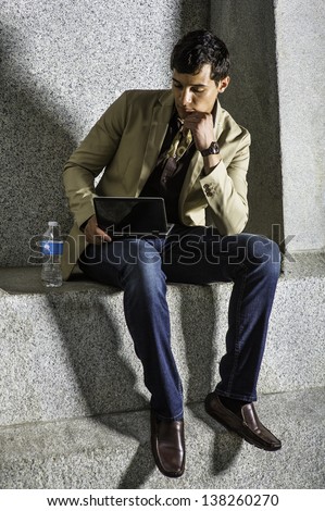 Sitting outside with a bottle of water, a young handsome businessman is  working on a small computer/Working Outside