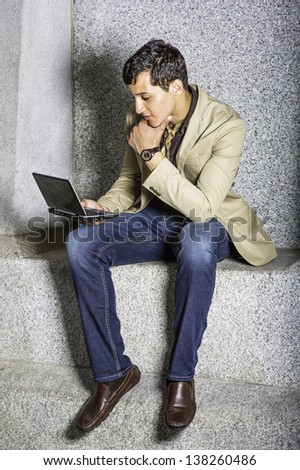 A young handsome businessman is sitting outside and working on a small computer/Working Outside
