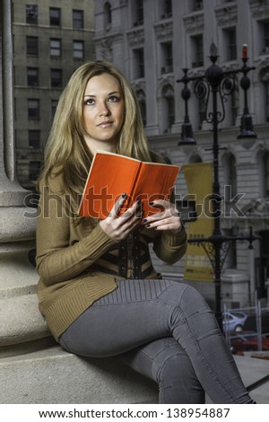 A young pretty woman is reading a red book outside./Reading Outside