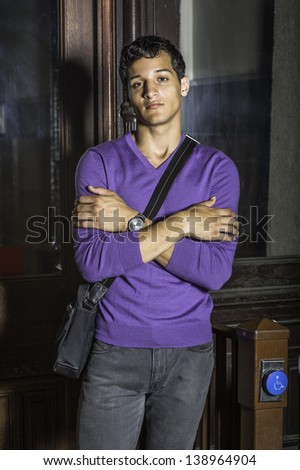 Carrying a bag and wearing a purple sweater, a young handsome student is crossing his arms and standing outside a office building in early morning./Portrait of Young Student