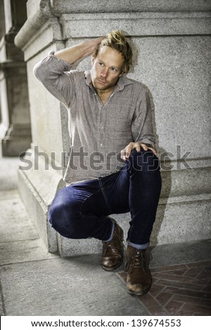 A young handsome guy is squatting outside, scratching his hair and thinking/Thinking Outside