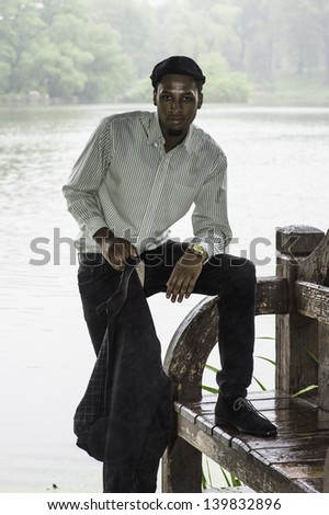 In a rainy day a young handsome black guy is standing by a foggy lake and relaxing