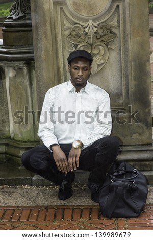 In the raining, a young handsome black traveler is squatting there and into deeply thinking/Thinking Outside
