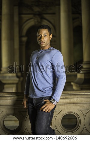 A young handsome black guy is standing at a hallway and looking at you./Portrait of Young Black Guy