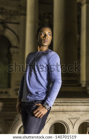 A young handsome black guy is standing at a hallway and looking forward./Portrait of Young Black Guy