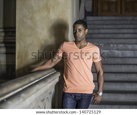 A young handsome black guy is standing at a hallway and seriously looking at you./Portrait of Young Black Guy