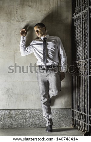 a young handsome black businessman is standing outside a gate and into deeply thinking./Lock Out