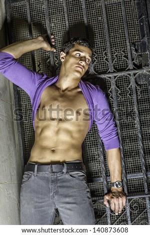 Leaning on a metal gate, a sexy young guy is  rolling his sweater over his head, showing his well defined body./Summer Heat