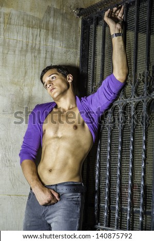 Leaning on the corner between a wall and a metal gate, a sexy young guy is  rolling his sweater over his head, showing his well defined body and into deeply thinking./Summer Heat