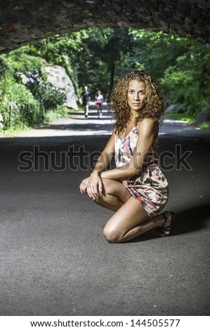 A fitness instructor with long brown curly hair, dressing in a skirt,  squats outdoor to demonstrate/Portrait of a female fitness instructor
