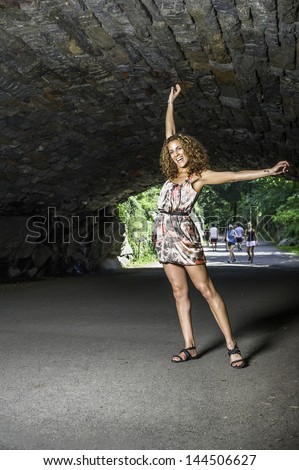 A fitness instructor with long brown curly hair, dressing in a skirt and under a shade,  is stretching two arms to demonstrate/Portrait of a female fitness instructor
