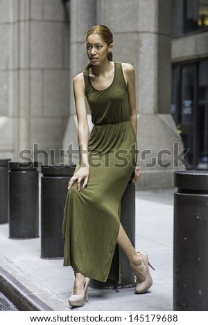 Dressing in a green Maxi Tank Dress,  a young black girl is sitting on black metal columns outside a building and relaxing. /Relaxing Outside