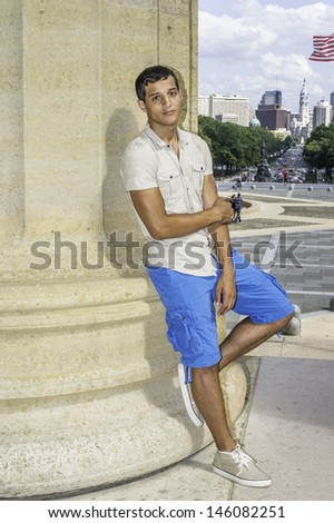 Dressing in a iron short sleeve shirt, blue shorts, a young attractive guy is standing by a column and charmingly looking at you. /Portrait of Young Guy
