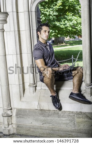 Dressing in a short sleeve shirt, pattern shorts and black leather sneakers, a young handsome student is sitting on a old fashion window frame and study on a computer in a campus / Study by Window