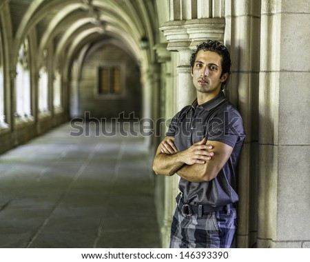A young strong handsome guy is standing by a old fashion hall way, crossing arms and thoughtfully looking at you. / Portrait of Young Guy