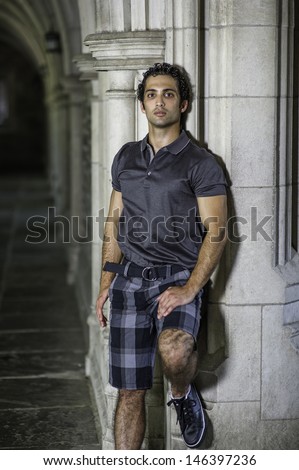 Dressing in a gray polo shirt, pattern shorts, a young strong handsome guy is standing by a old fashion wall, confidently looking forward. / Portrait of Young Fitness Guy
