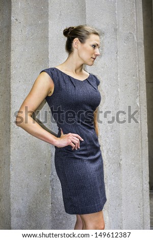 Dressing in a sleeveless work wear dress and with a tight top knot bun, a young pretty businesswoman is standing outside and taking a break. / Portrait of Businesswoman