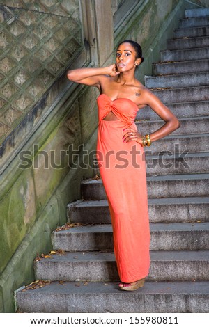 Dressing in a contemporary style red strapless long dress,  a young pretty girl is standing on steps, charmingly looking at you /Lady on Steps