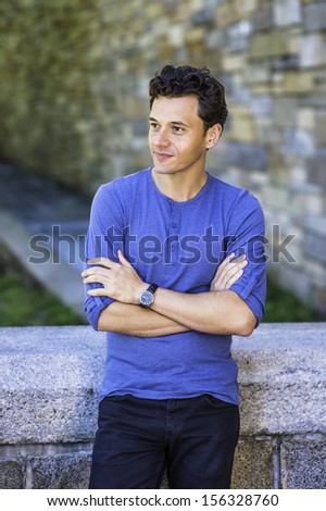 Dressing in a blue long sleeves with roll-tab Henley shirt, wearing a wristwatch, crossing arms,  a young handsome guy is relaxing outside. / Relaxing Outside