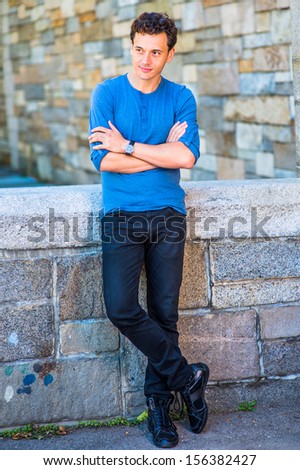 Dressing in a blue long sleeves with roll-tab Henley shirt, black jeans, leather sneakers, wearing a wristwatch, crossing arms,  a young handsome guy is relaxing outside. / Relaxing Outside