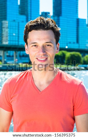 Dressing in a light red T shirt, a young handsome guy is standing by the river, smilingly looking at you. / Portrait of Young Guy