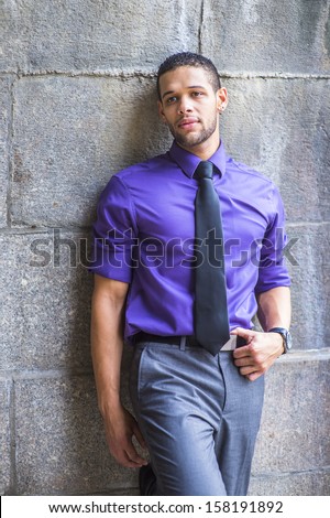 Dressing in a purple shirt, gray pants and a black tie, a young handsome student with a little beard and mustache is leaning against the wall, thinking outside. / Portrait of Young Handsome Student
