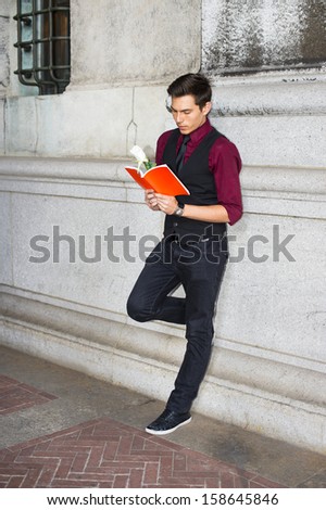 Dressing in a red shirt, a black vest, black jeans and a black tie, a young handsome guy is reading a red book with a white rose. / Reading Outside