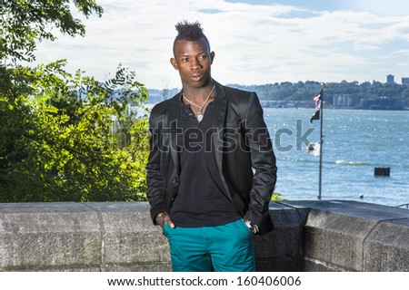 Dressing in a black blazer, a black undershirt and green pants,  two hands putting in pockets, a young black guy with mohawk hair is standing by a river, relaxing and thinking. / Relaxing Outside