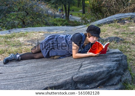 Dressing in a blue sleeveless long blouse, black leggings and boots, wearing a black corduroy cop, a young Chinese girl is lying on rocks, reading a red book. / Reading Outside