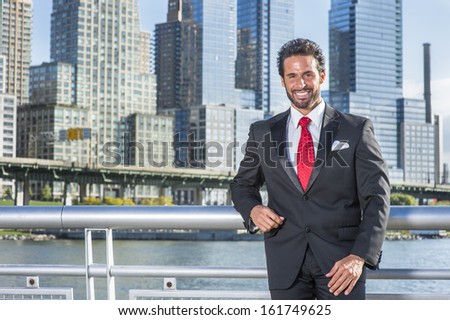 Dressing is a black suit, red tie, a handsome, sexy, middle age businessman with mustache and beard is standing in the front of a business district, smilingly looking at you. / Portrait of Businessman