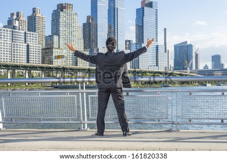 Facing dramatic high buildings of New York City, a middle age businessman is raising both arms, a symbol of success. / Welcome Home