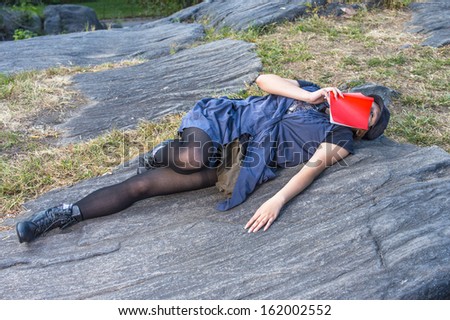 Dressing in a blue sleeveless long blouse, black leggings and boots, wearing a black corduroy cop, a young Chinese girl is lying on rocks, a red book covering her face, relaxing / Relaxing on Rocks