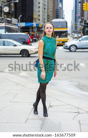 Dressing in green and black patterned sleeveless dress, black leggings, leather shoes and a black waist strap, a happy girl is standing on a busy street of a big city. / Tourist,
