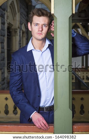 Dressing a blue jacket and light blue under shirt, a young handsome guy is standing by a column at a cottage,  sincerely looking at you / Portrait of Young Guy
