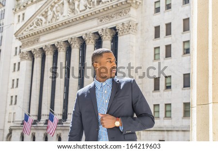 A young black businessman is standing outside an office building, confidently looking forward. / Portrait of Young Black Businessman