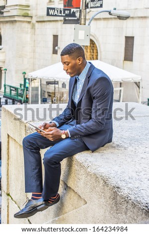 Dressing in a blue suit and leather shoes, a young black businessman is sitting outside, reading on a tablet computer. / Reading Outside