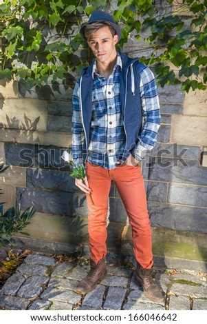 Dressing in a blue and white pattern shirt, a blue hoodie vest,  red jeans and brown leather boot shoes, wearing a woolen Fedora hat, a young handsome guy is holding a white rose and waiting for you.