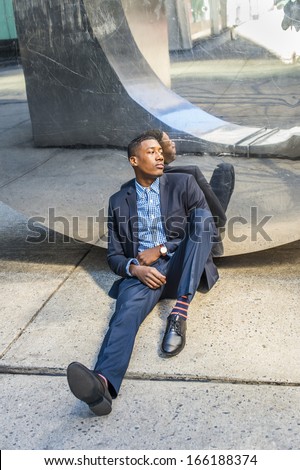 A young black businessman is tired, sitting on the ground, leaning against a modern mirror wall, relaxing and thinking. /Difficult Time