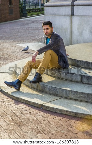 A young handsome Middle Eastern guy with bread and mustache is sitting on circle steps, relaxing and thinking. There is a pigeon on the background. /Seeking Peace