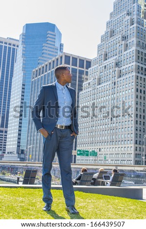 A young black businessman is standing in the front of a busy business district, looking around and taking a break. / Looking forward,