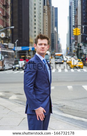 Dressing in a blue slim fit suit and patterned tie, a young handsome businessman is standing on a busy street in a big city. / Portrait of Young Professional
