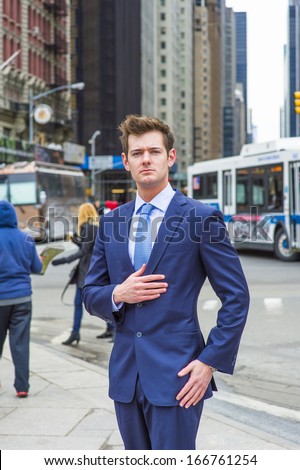 Dressing in a blue slim fit suit, patterned tie and light blue under shirt, a young handsome businessman is standing on a street in a big city. / Traveling Businessman