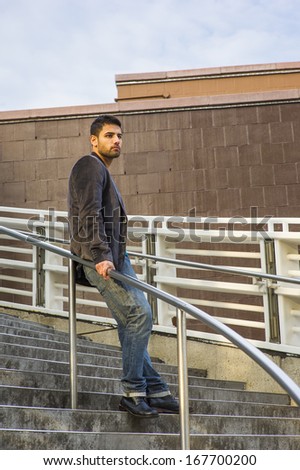 Dressing in dark purple woolen blazer, jeans and leather shoes, a young guy with beard and mustache is standing against a metal railing on stairs, under sunshine of sunset, thinking. /Thinking Outside