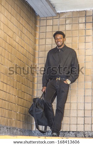 Dressing in a waterproof jacket, a ivy cap, carrying a traveling bag, a young handsome black guy is walking down on the station. / Traveler