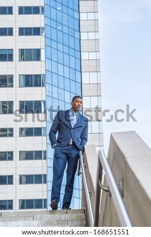 A young handsome black businessman is standing outside of a business building, relaxing and thinking.
